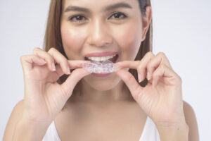 Woman holding clear aligners near her mouth showing can I drink tea with Invisalign concerns during treatment