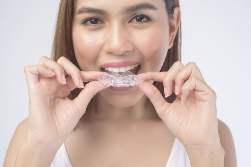 Woman holding clear aligners near her mouth showing can I drink tea with Invisalign concerns during treatment